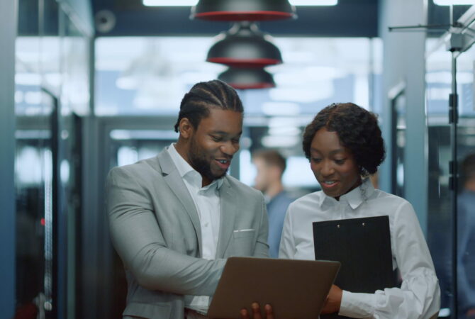 Portrait of smiling partners using laptop in corridor. Couple discussing project